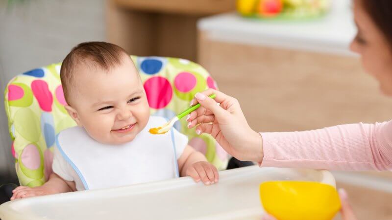 cheerful-baby-eating-in-kitchen-in-high-chair